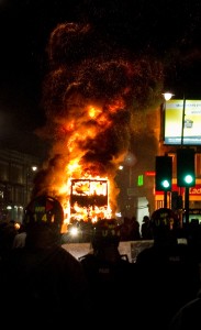 A double decker bus burns as riot police